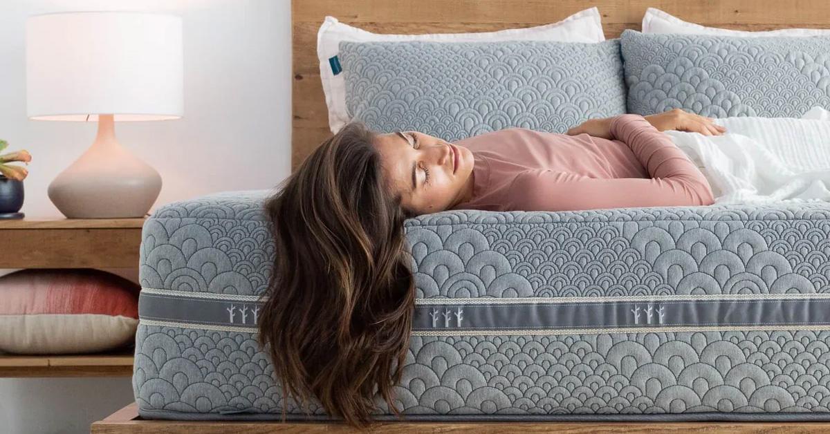 woman with long hair lying on mattress in bedroom with nightstand and lamp