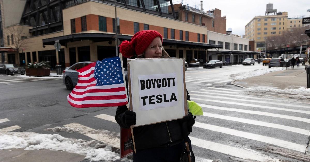 A woman holds a boycott tesla sign and an American flag while protesting Elon Musk's company