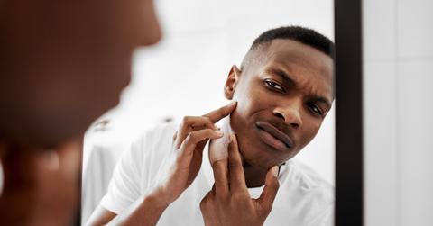 A young man popping pimples in the bathroom mirror.