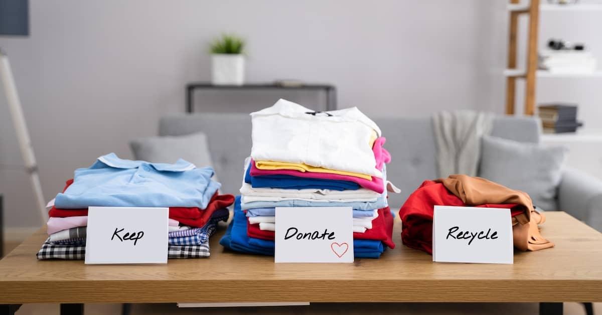 Three piles of clothes on a table, with paper signs saying, keep, donate and recycle on them.