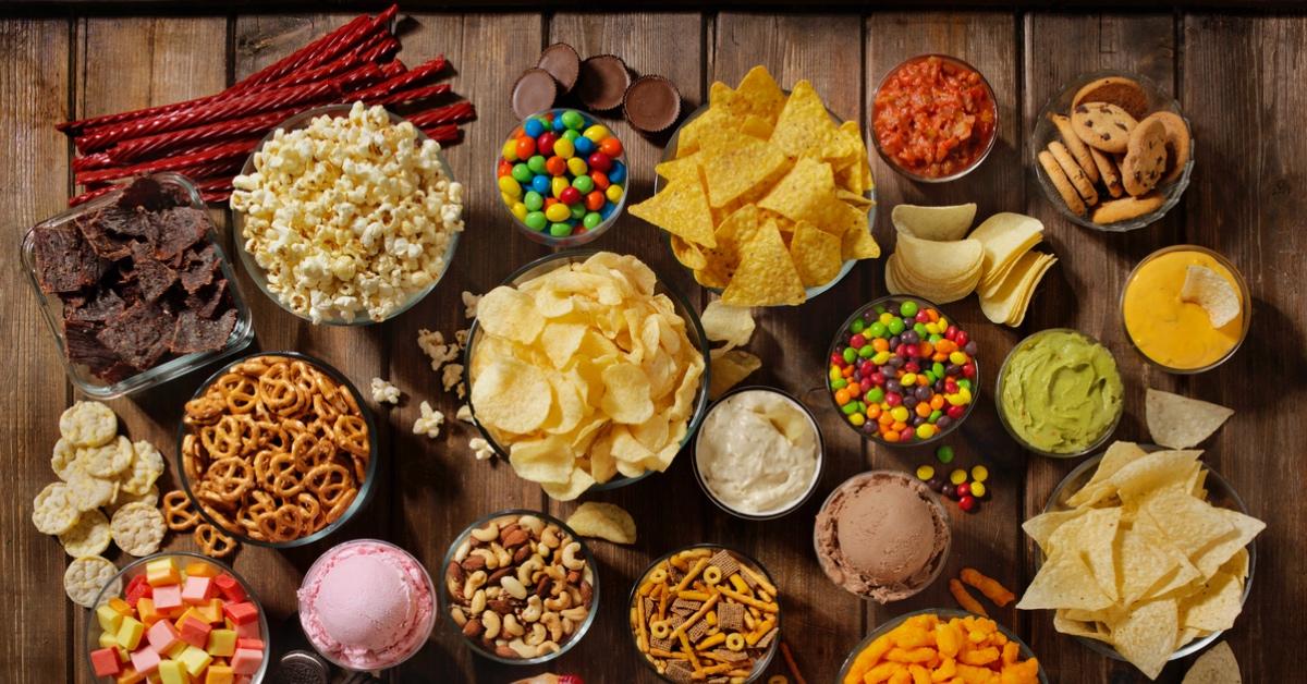 Table full of ultra-processed foods such as potato chips, pretzels, ice cream, and candy. 