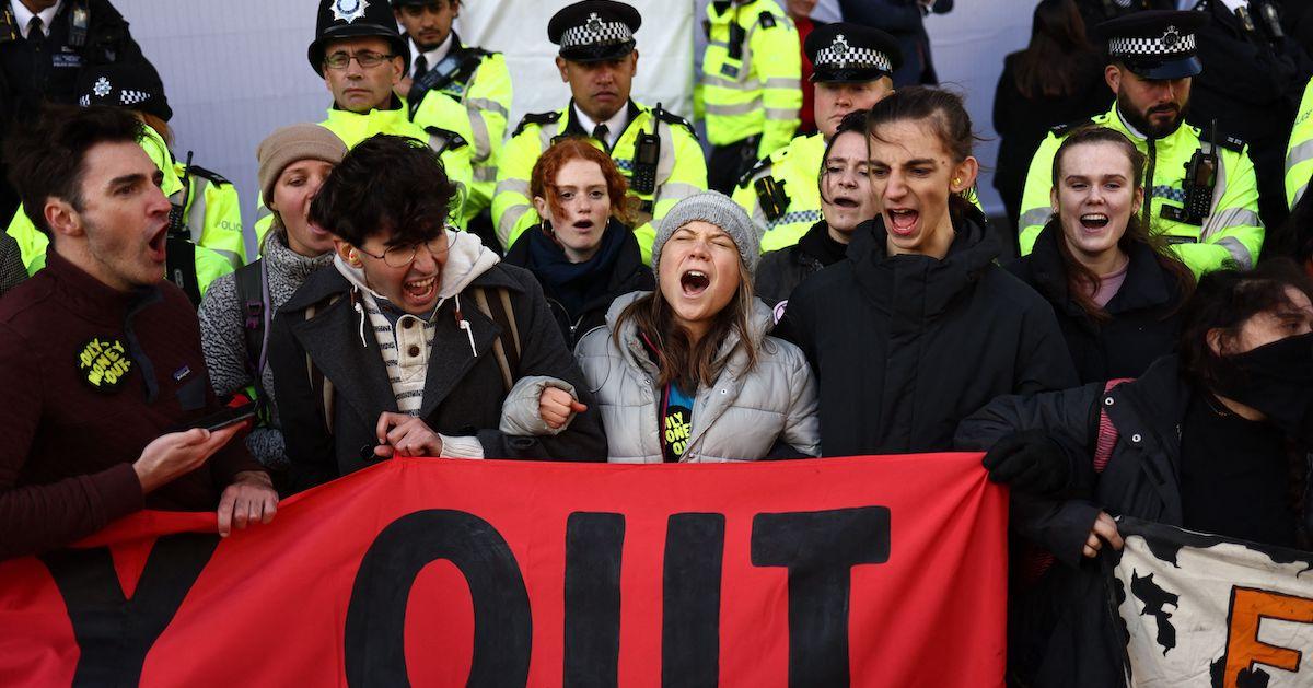 Greta Thunberg chants at protest with other activists, holding banner, with police behind them