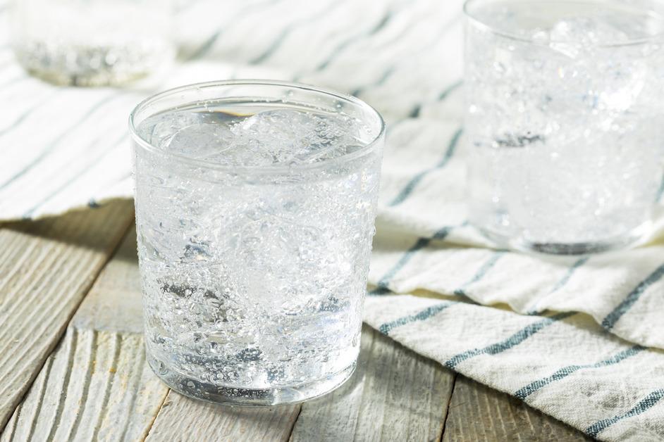 Two glasses of sparkling water with ice sit on a wooden table covered with a striped table cloth.