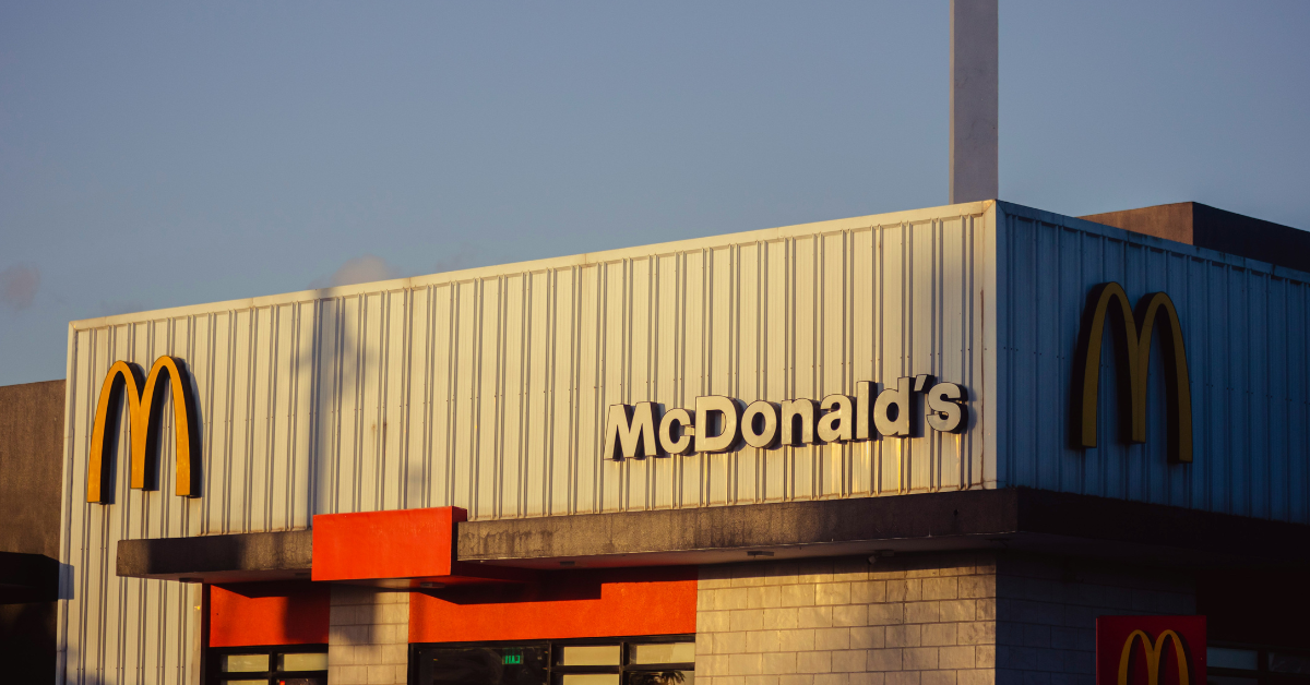 The front of a McDonald's is partially hidden in the shadows on a sunny day