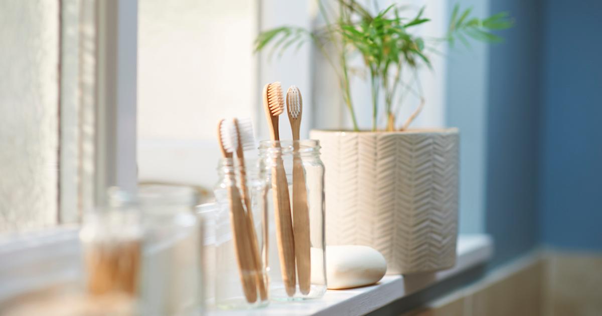 Bamboo toothbrushes in a glass jar on a bathroom counter.