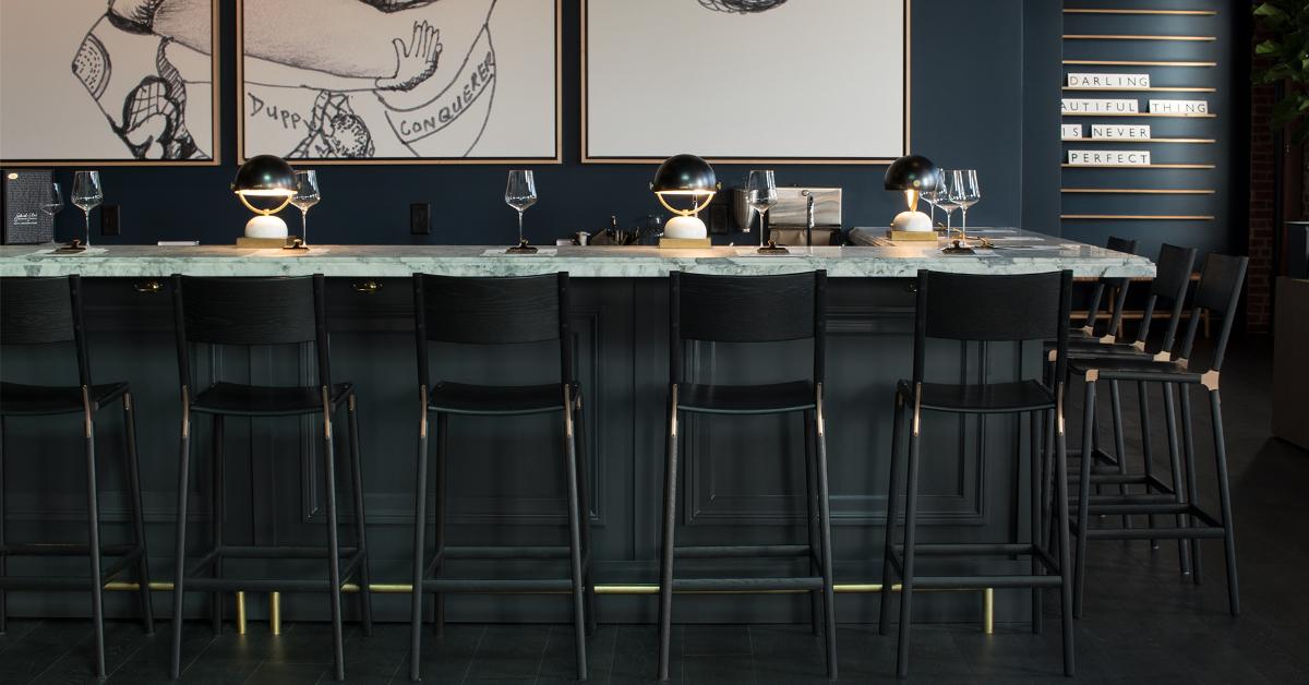 Photo of black wood Fyrn chairs lined up against a marble top bar 