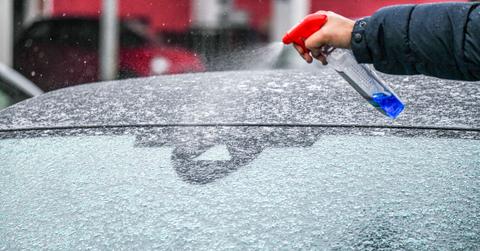 Hand sprays a spray bottle onto an icy windshield
