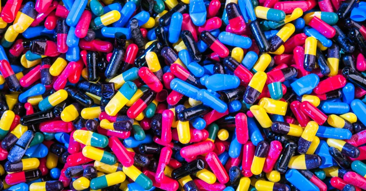 Close-up photograph of brightly colored pills in magenta, black, teal, and yellow.