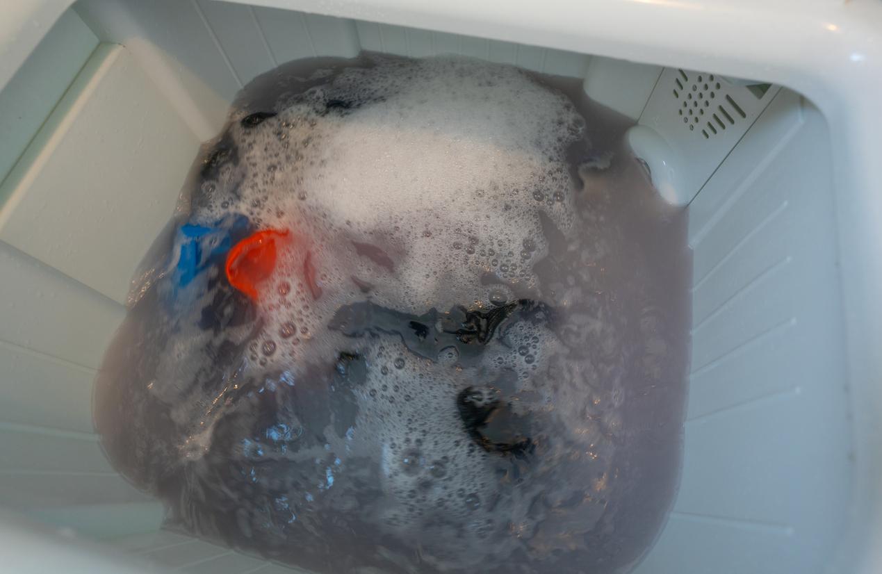 Items submerged in dirty, gray water inside a large washing basin. 