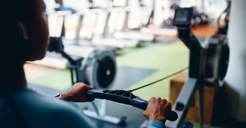 A woman uses a rowing ergometer in a gym with the handle in the foreground.