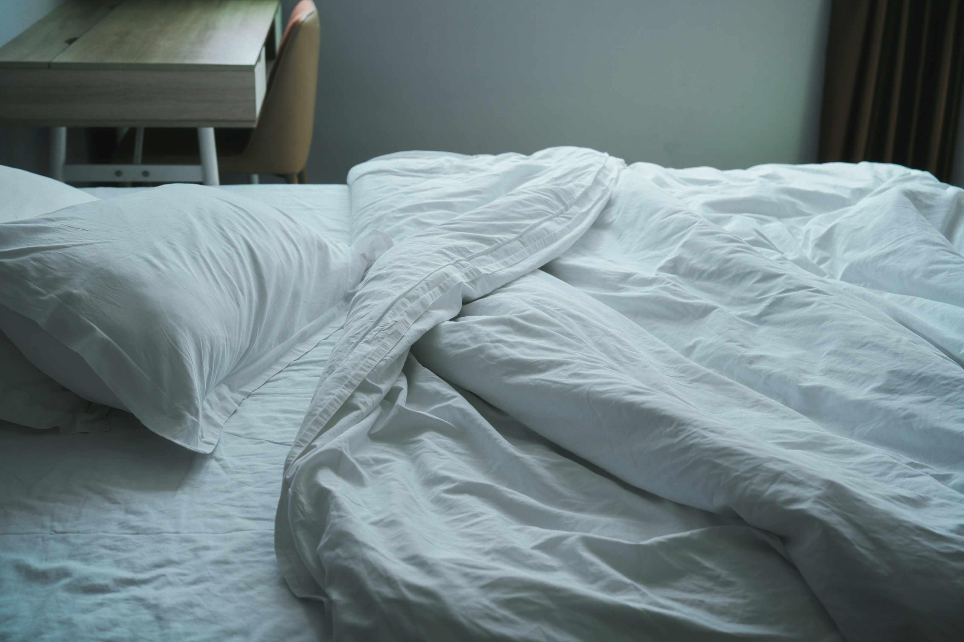 An unmade bed with white pillows and a white sheet and blanket is pictured.