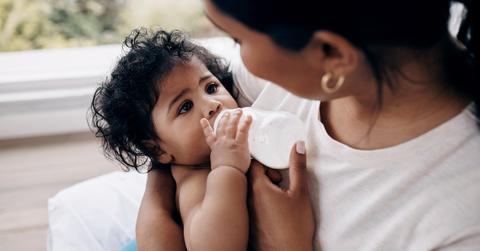 A baby drinks from a bottle and gazes up at their mother.