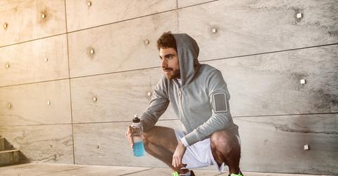 A man on a run crouches on the ground while holding a blue drink.