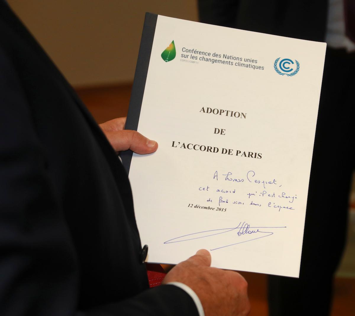 Person holding a copy of the signed Paris Agreement with a handwritten note on the front.