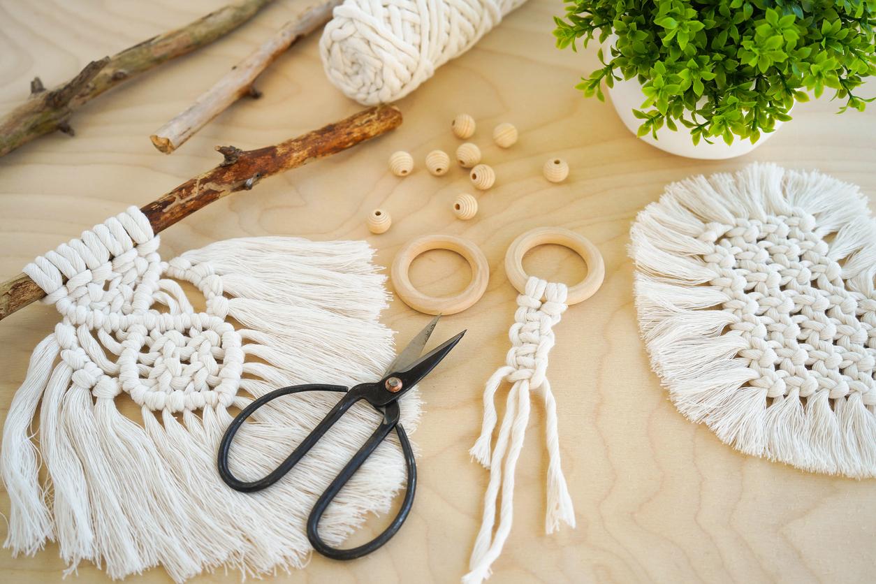 Various macrame projects and supplies scattered on a light-colored wood table.