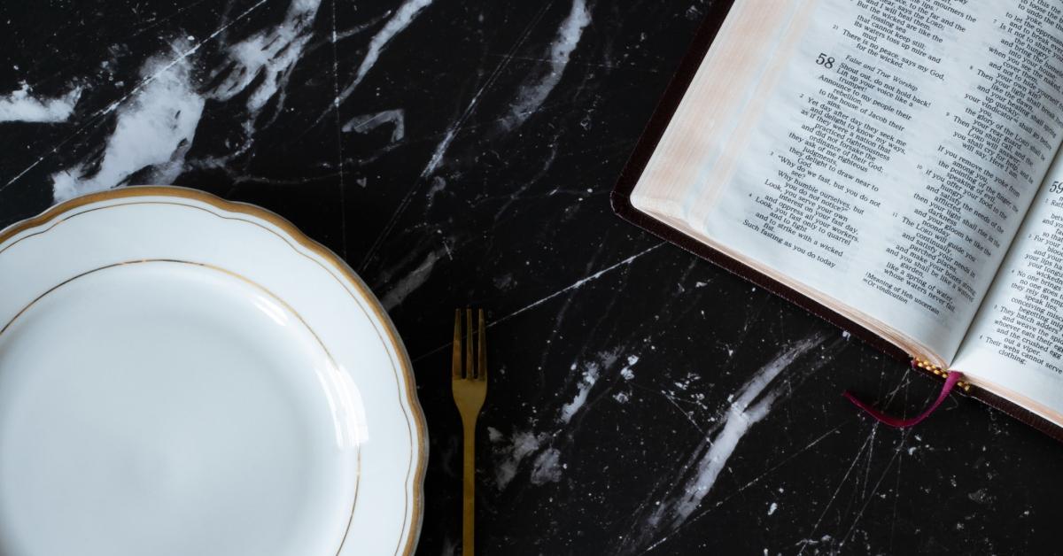 An empty plate and a golden fork sits on a black granite countertop next to an open Bible. 