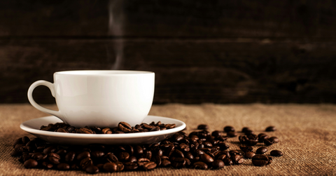 A white coffee mug steams while sitting on a pile of coffee beans