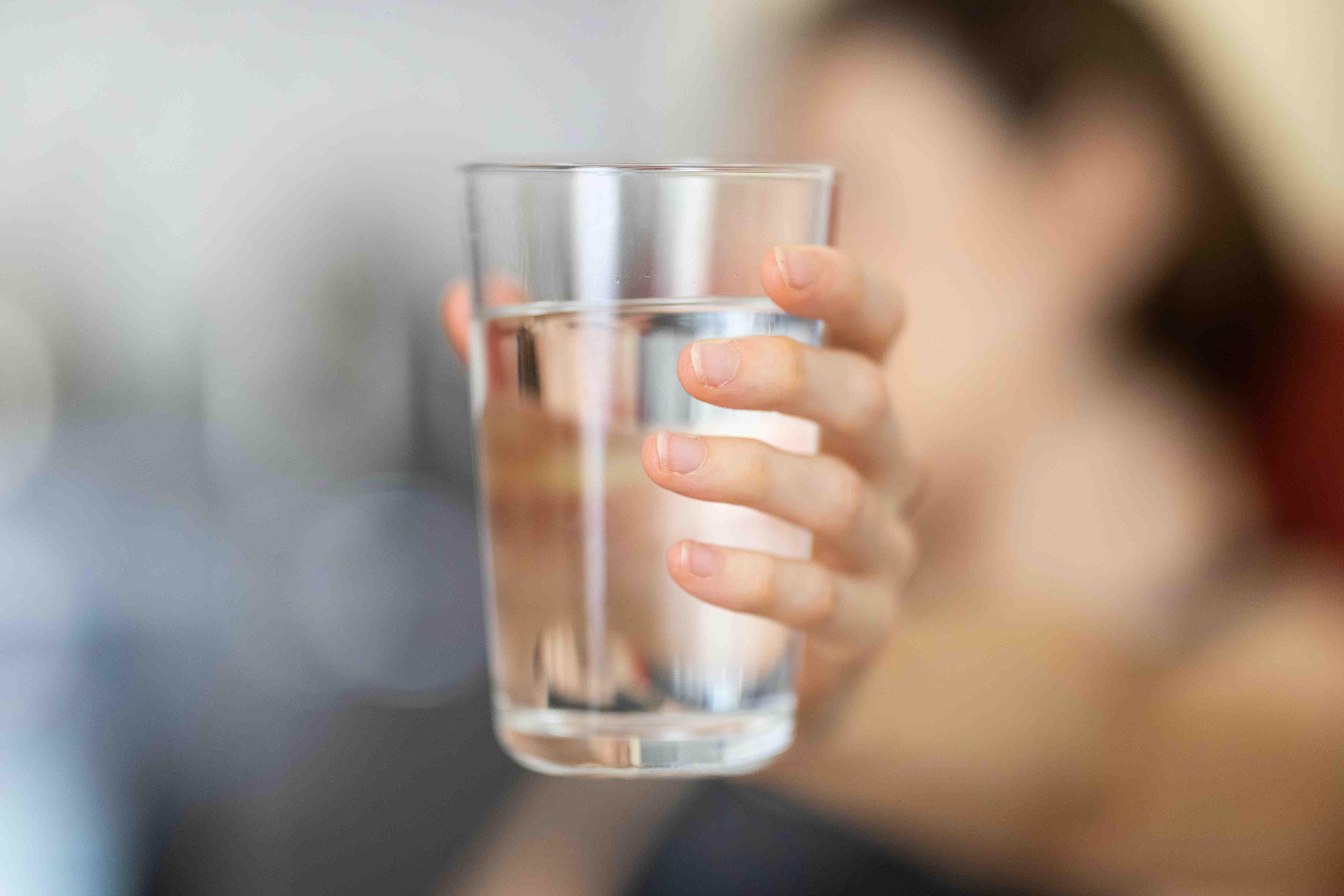 A person holds out a glass of water with their arm extended.
