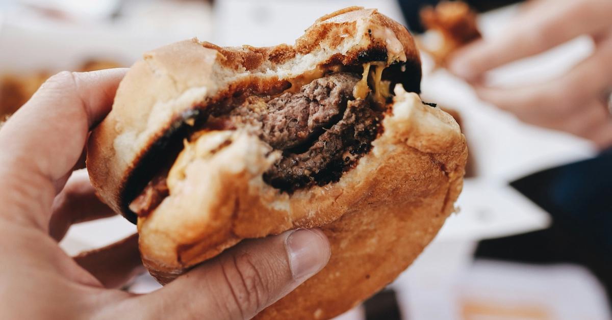 Close up photograph of a person holding a hamburger that has a bite taken out of. 