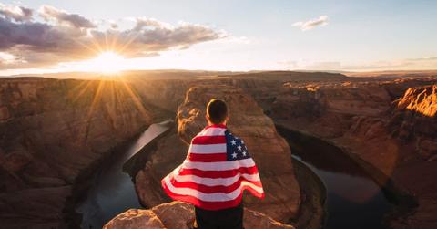Young man at a national park viewpoint wrapped in the American flag. (Representative Cover Image Source: Getty Images | Westend61)