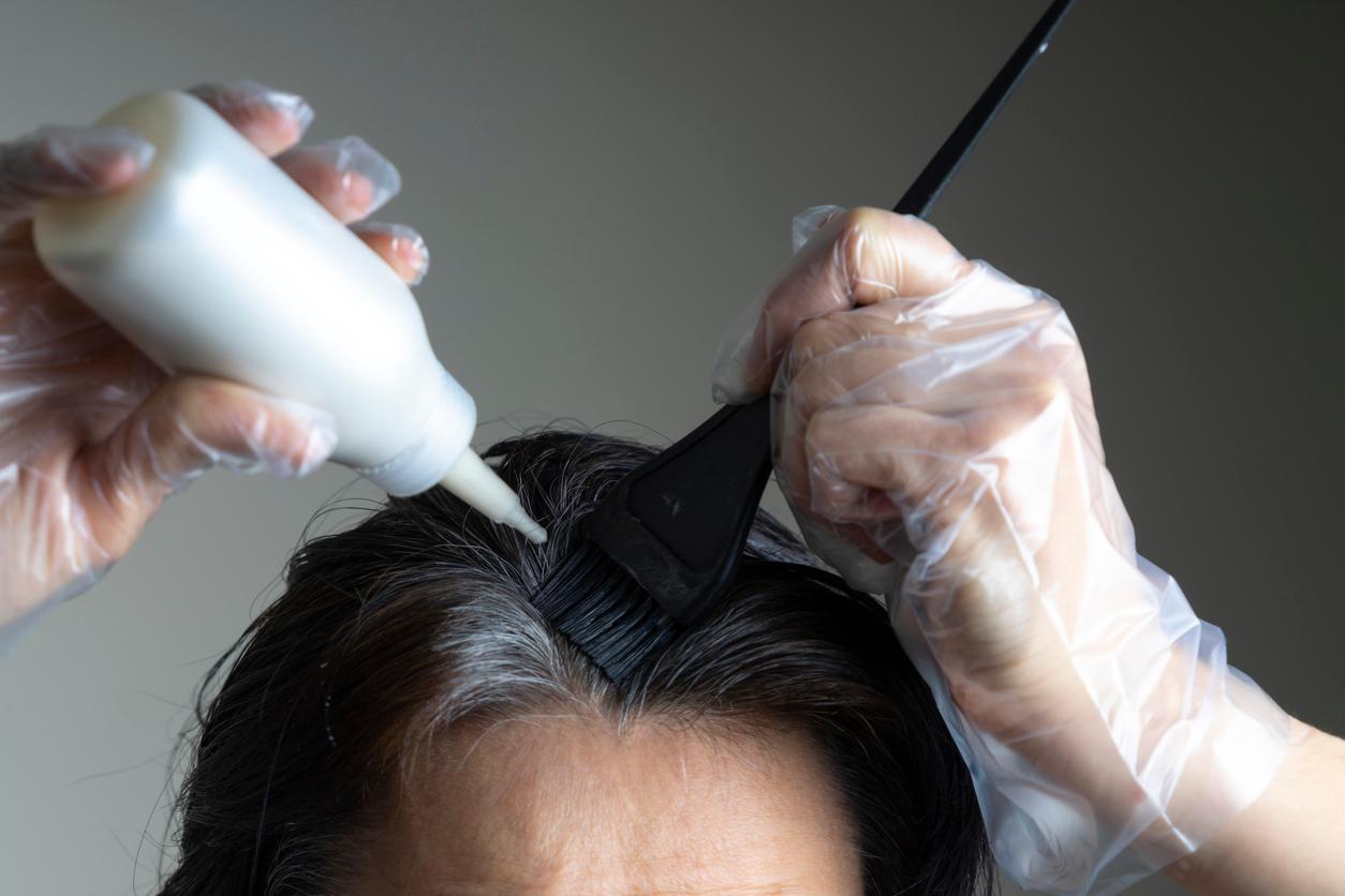 An individual places hair dye from a squirt bottle in their hair while brushing it through with a black brush.