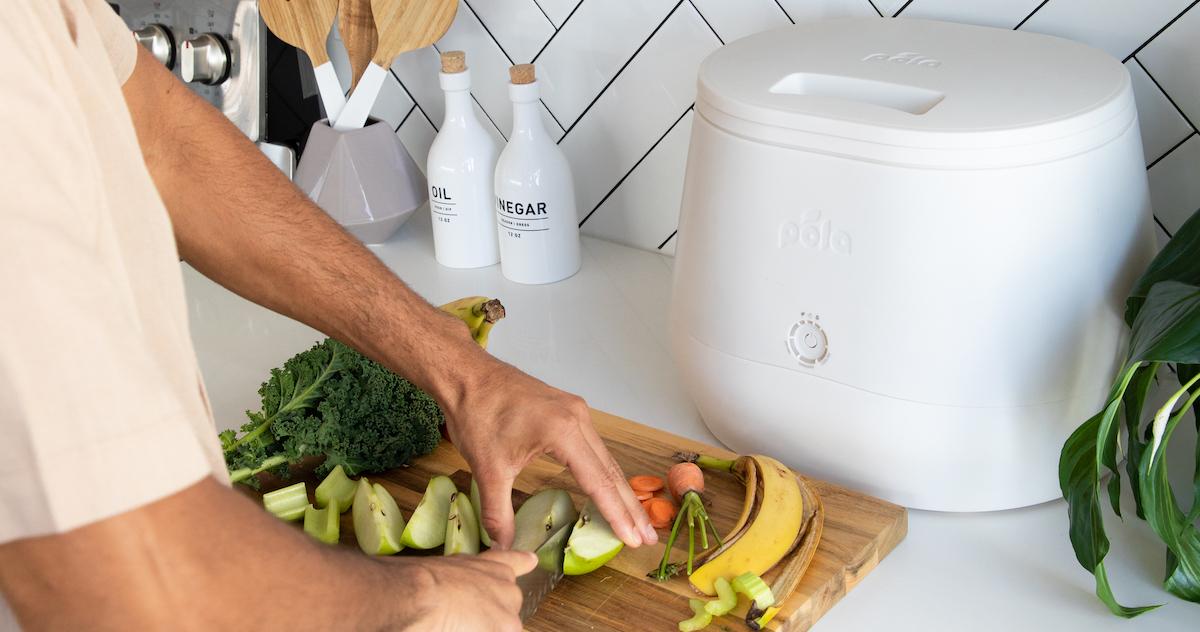 Hands are seen chopping fruit at a kitchen counter beside a white Lomi composting machine.