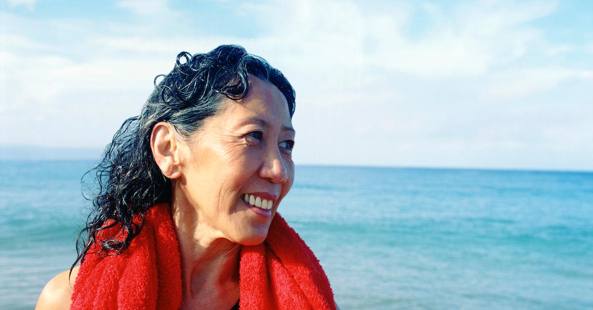 Woman smiles on a beach, with a red towel around her neck