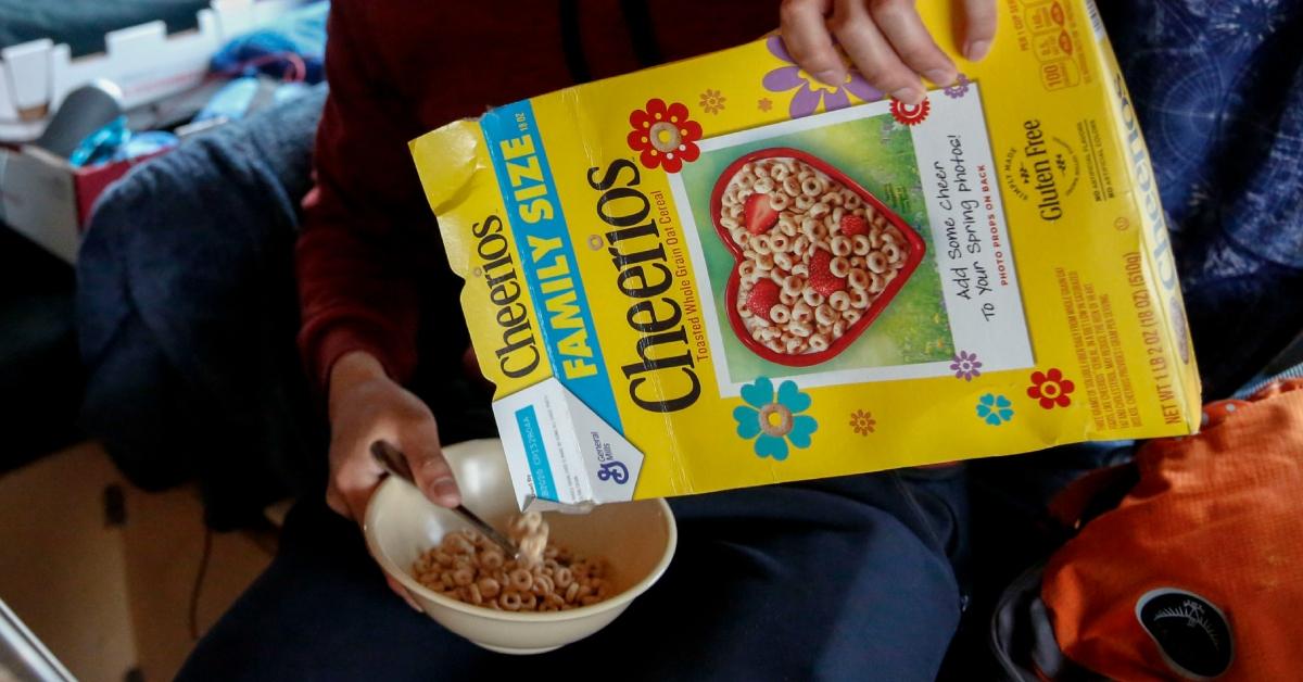 A person pours a Cheerios into a bowl from a Family Size box.