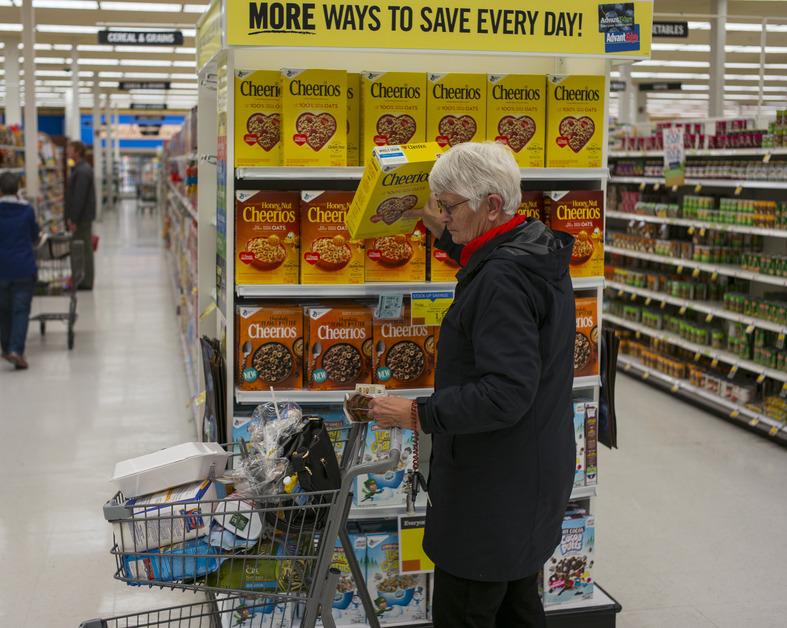 A woman shopping at the grocery store pulls a box of plain Cheerios off the shelf. 