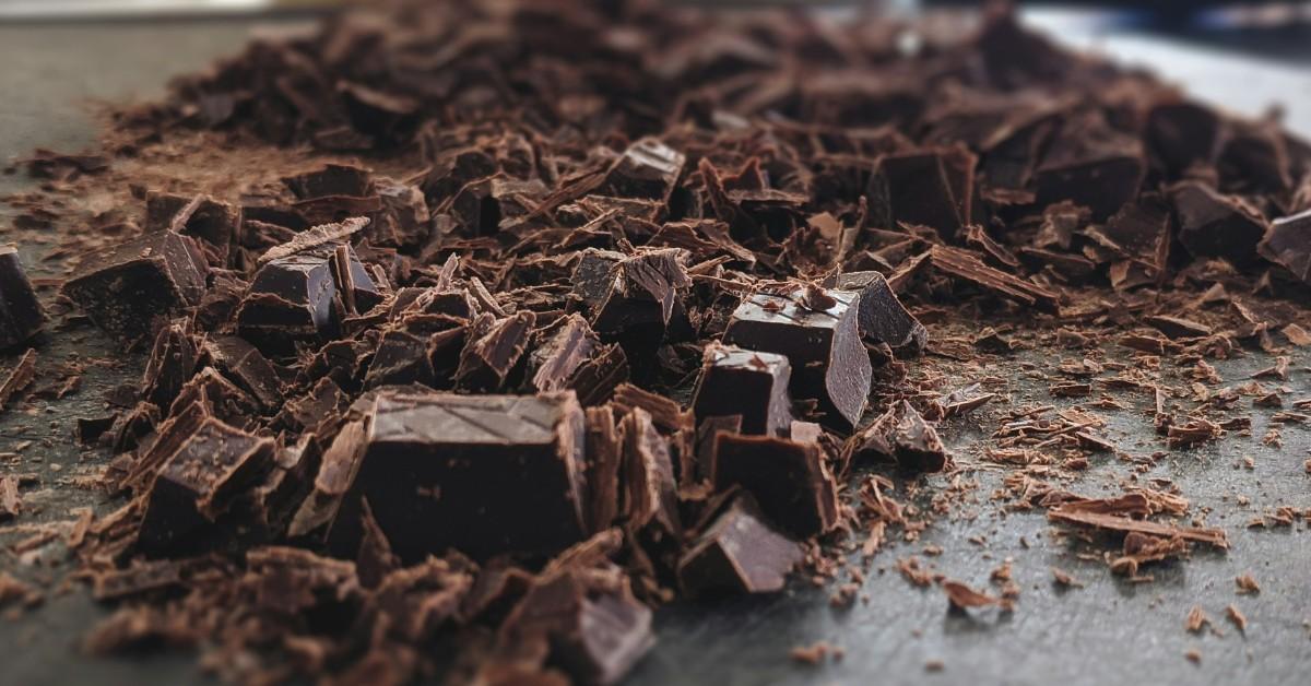 A pile of chocolate chunks sits on a table, with a few larger pieces visible amongst the smaller bits