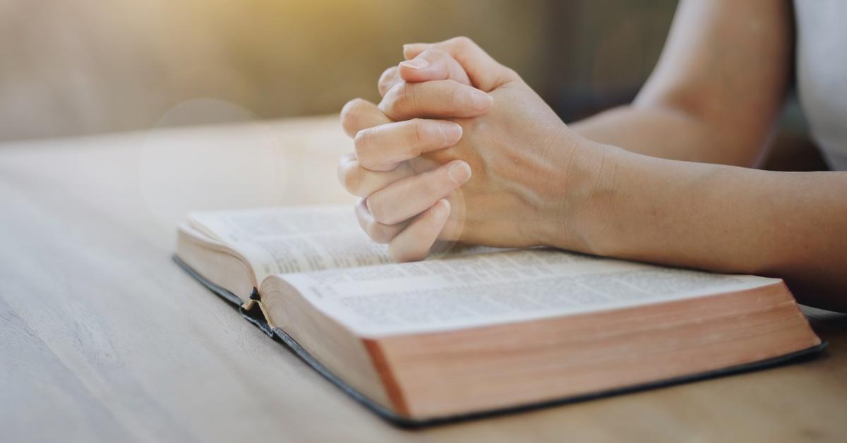 Person with their hands folded in prayer over a Bible. 