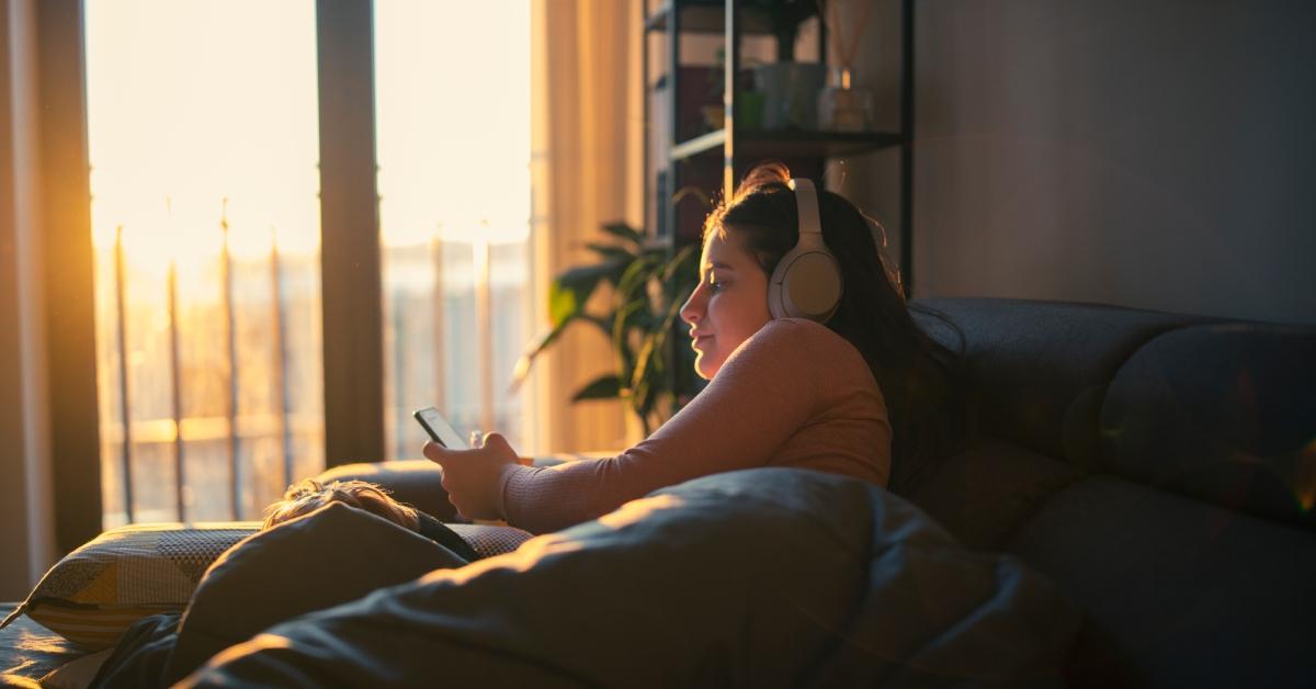 A woman sits on her couch during golden hour with headphones on.