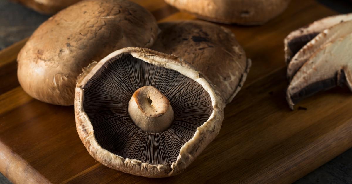 A portobello mushroom lies face up on a wooden cutting board among other portobello mushrooms. 