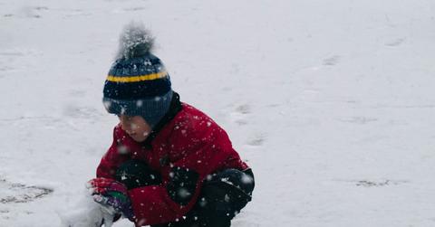 A young boy squats in the snow as he makes a snowball.