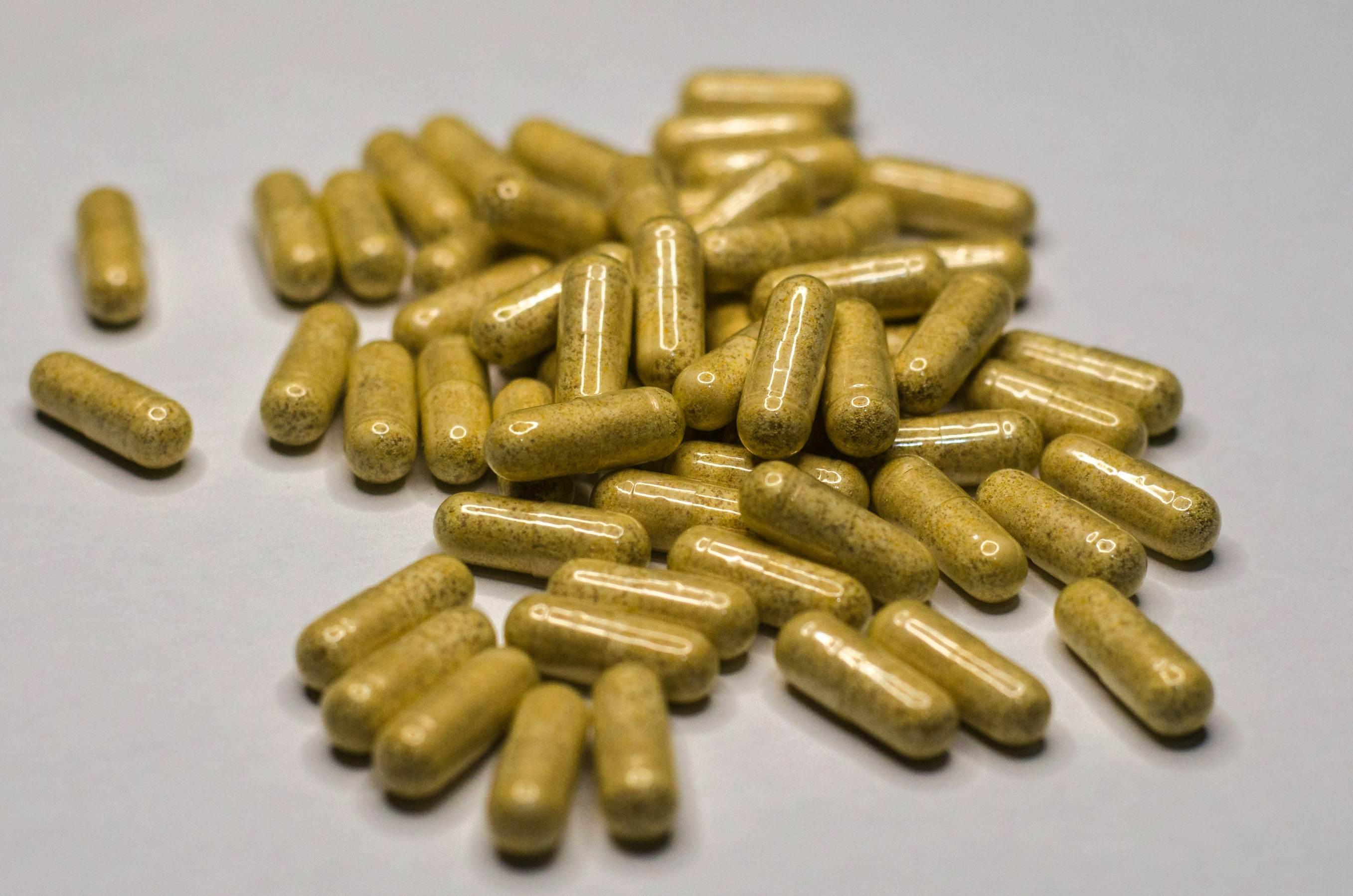 Green herbal supplements are contained within clear capsules stacked atop one another.