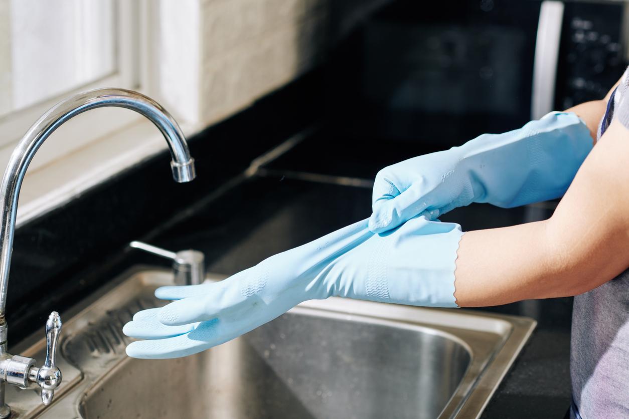 An individual pulls on two reusable rubber gloves before cleaning dishes in the kitchen sink.