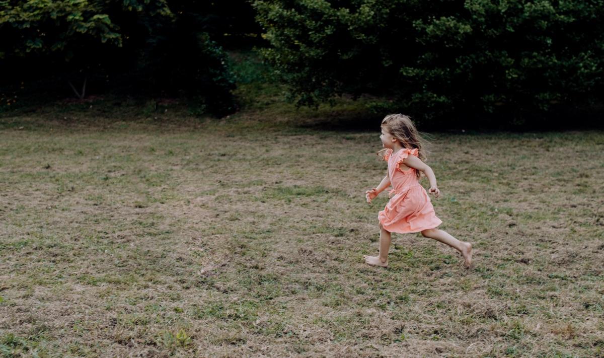 little girl in a peach dress running barefoot on grass