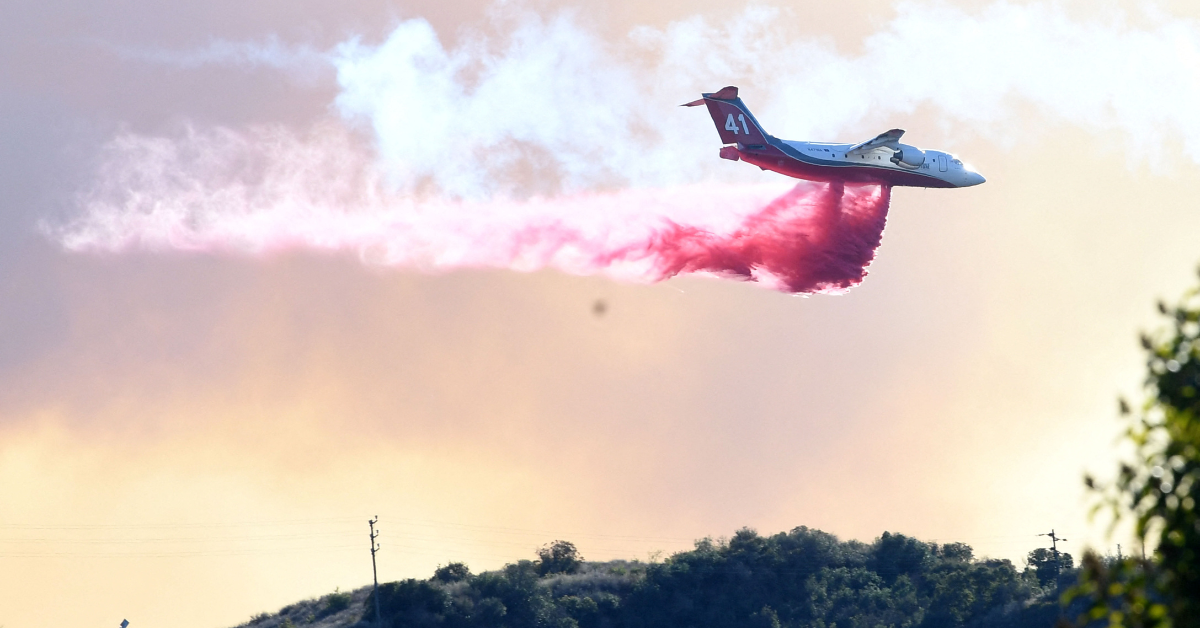 A plant flies overhead as it drops pink colored fire retardant over areas in L.A. County