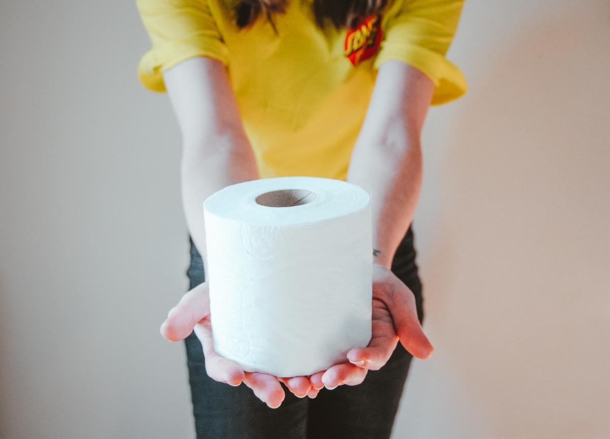 person in yellow tee holding out one roll of toilet paper