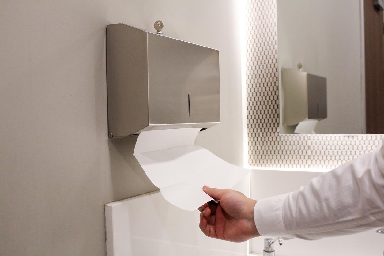 A person retrieves a paper towel from a sleek metal dispenser in a bathroom to dry his hands.