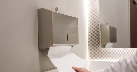 A person retrieves a paper towel from a sleek metal dispenser in a bathroom to dry his hands.