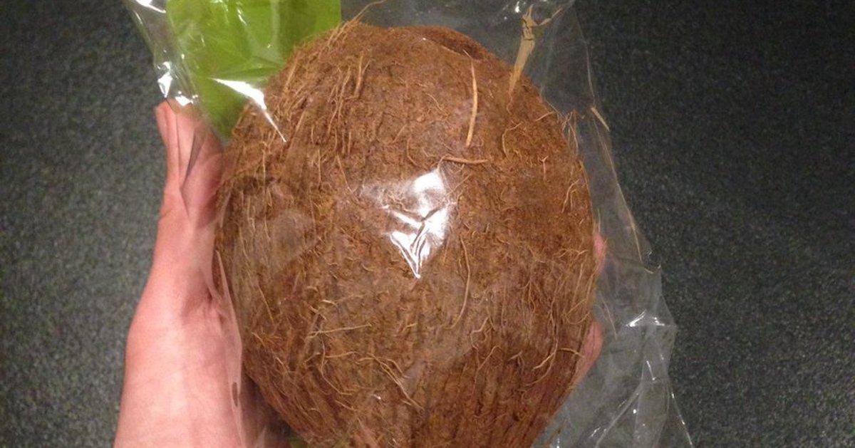 Hand holds a coconut wrapped in plastic bag