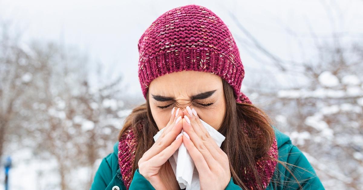 A woman in winter wearing a red hat blowing her nose.