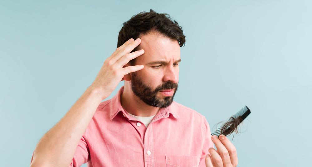 A man is looking at a comb concerned he's losing hair.