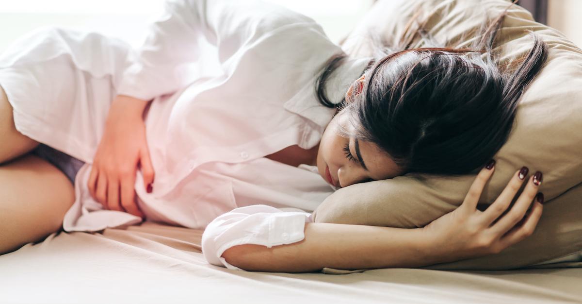 Woman lays on her side, clutching stomach