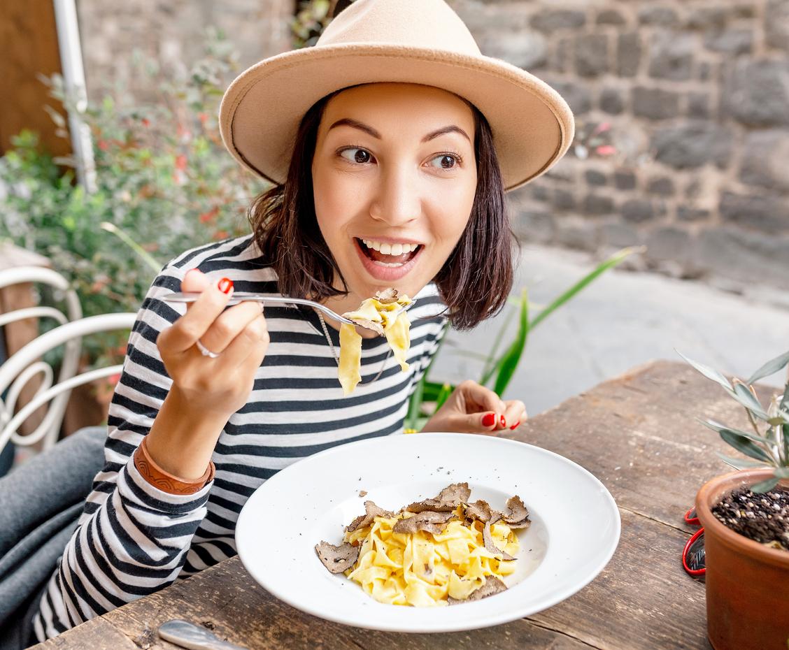 A woman in a striped shirt and hat eats pasta with truffles in Italy.