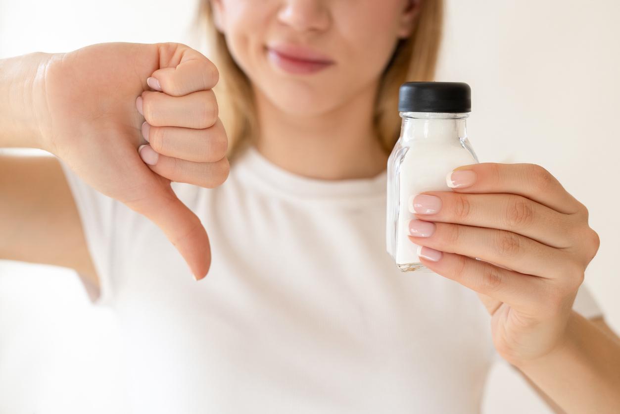 A woman holds a salt shaker in one hand and displays a thumbs down sign with her other hand.