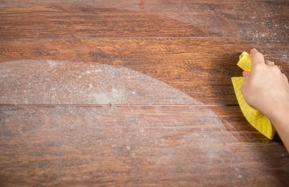 A person wipes dust off of hardwood floors using a yellow rag. 