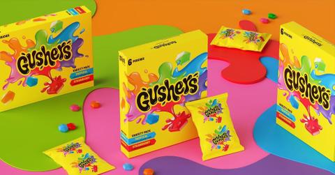 Three boxes of Gushers candy beside packets of Gushers with candy spilled around them.