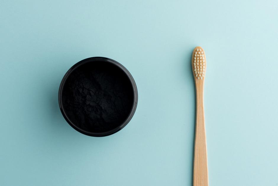 A bamboo toothbrush sits next to a black container on a blue background.